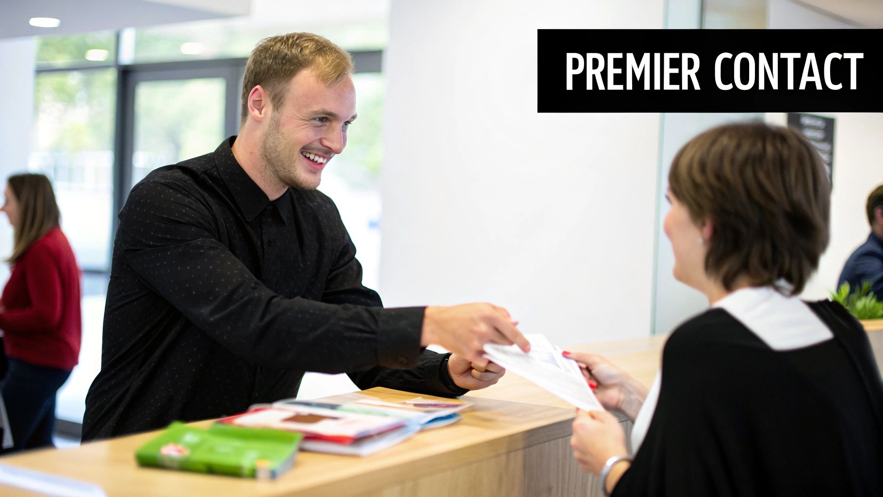 Un homme souriant remet des documents à une femme à un comptoir d'accueil. L'inscription « PREMIER CONTACT » est visible.