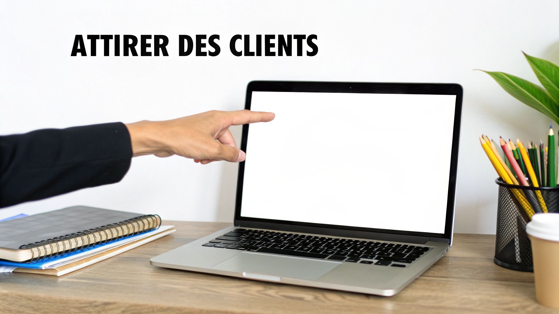 Une main pointe un écran d'ordinateur portable vide sur un bureau en bois, avec le texte "ATTIRER DES CLIENTS" affiché. Des fournitures de bureau sont également présentes.