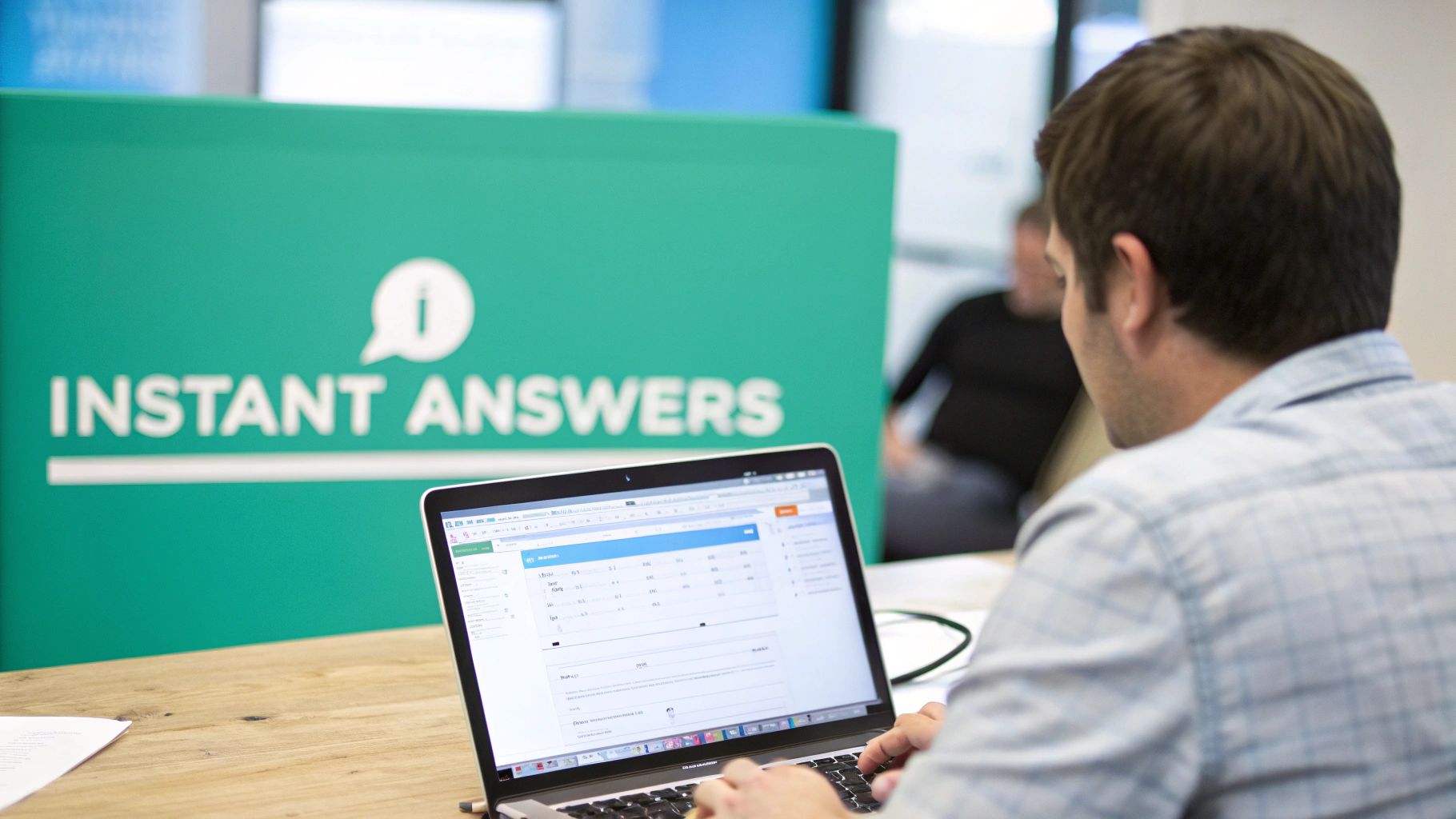 Man typing on a laptop in an office, with an 'Instant Answers' sign visible behind him.