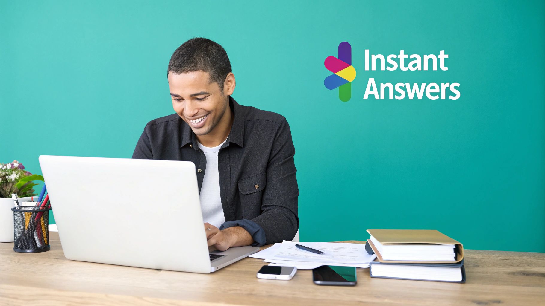 A smiling man works on his laptop at a desk with an "Instant Answers" logo on a green wall.