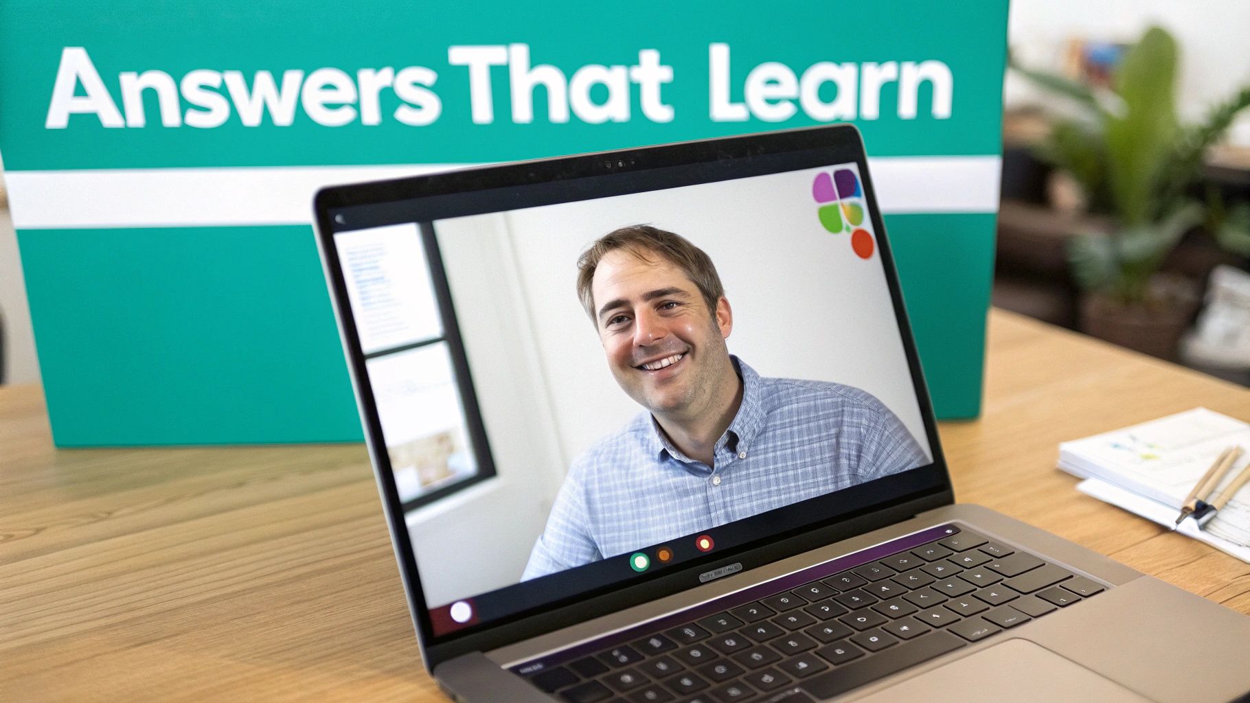 A smiling man is on a video call displayed on a laptop, with a green sign behind him.