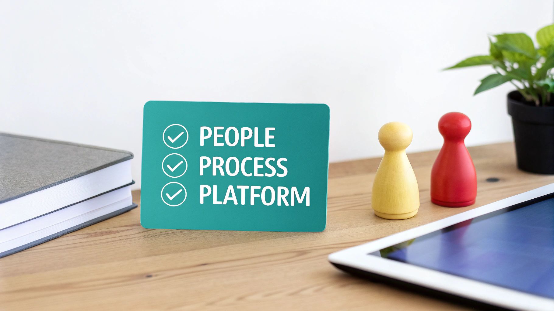 A teal sign on a wooden desk lists 'PEOPLE, PROCESS, PLATFORM' with checkmarks, next to books, game pieces, and a tablet.
