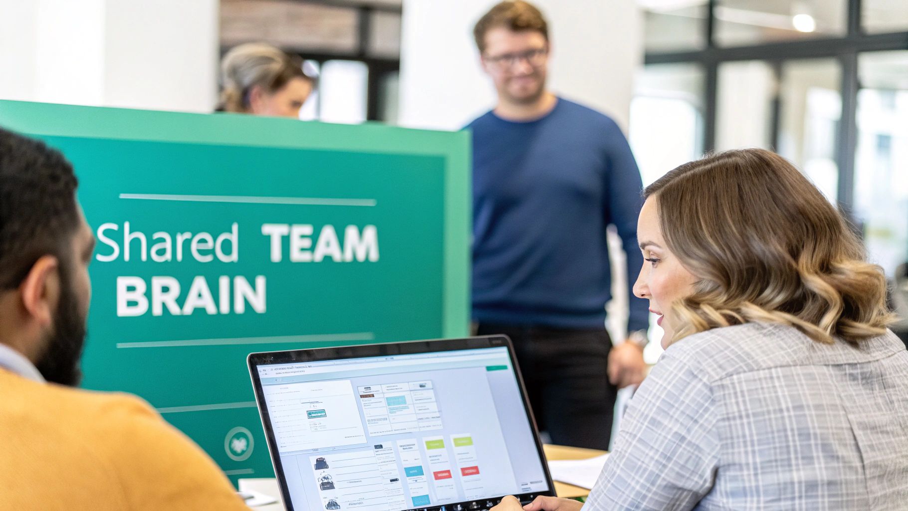 Two professionals collaborate in an office, using a laptop with a 'Shared TEAM BRAIN' sign in the background.