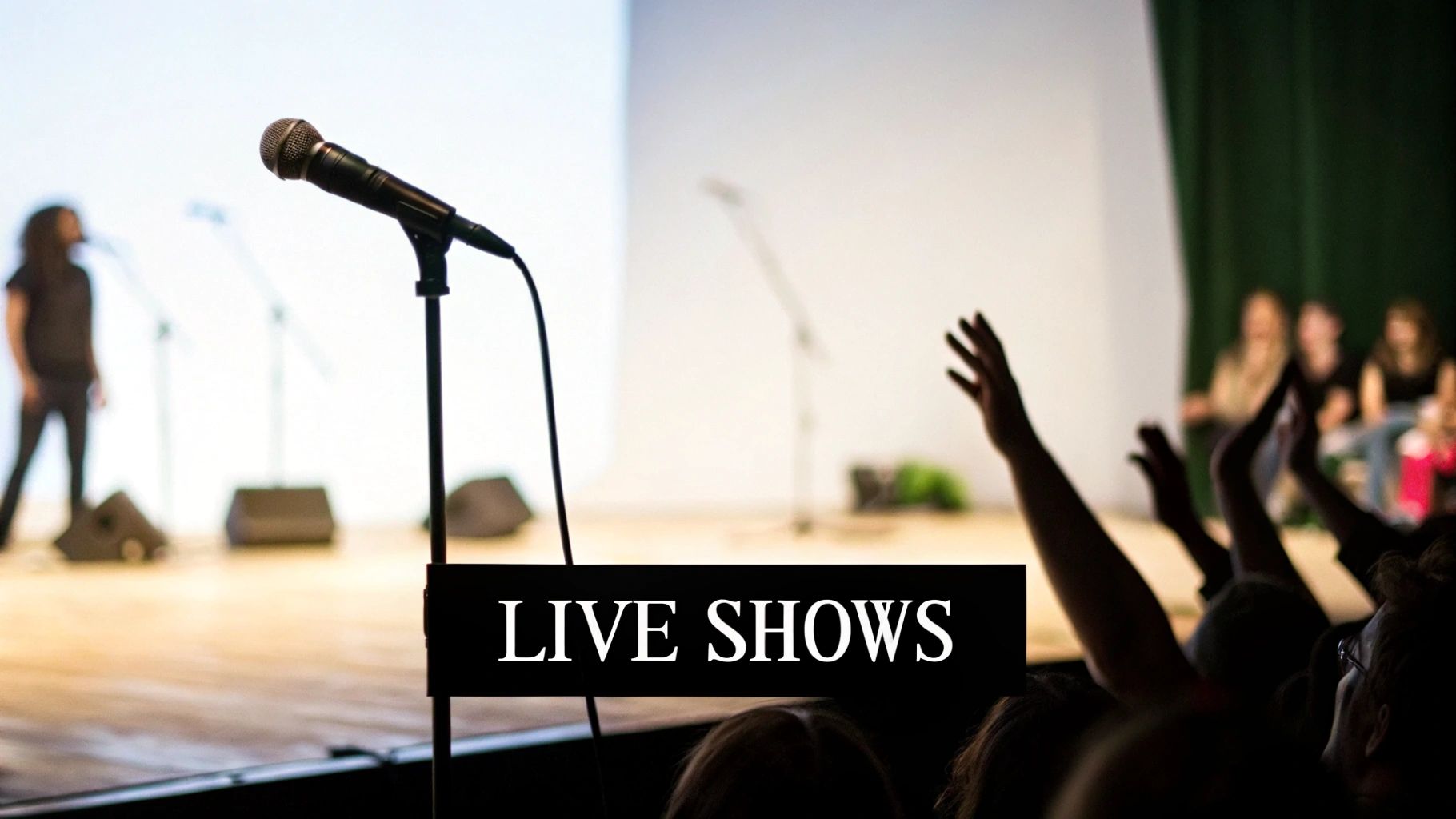 A live show with a microphone on stage, a blurred performer, and an audience with raised hands.