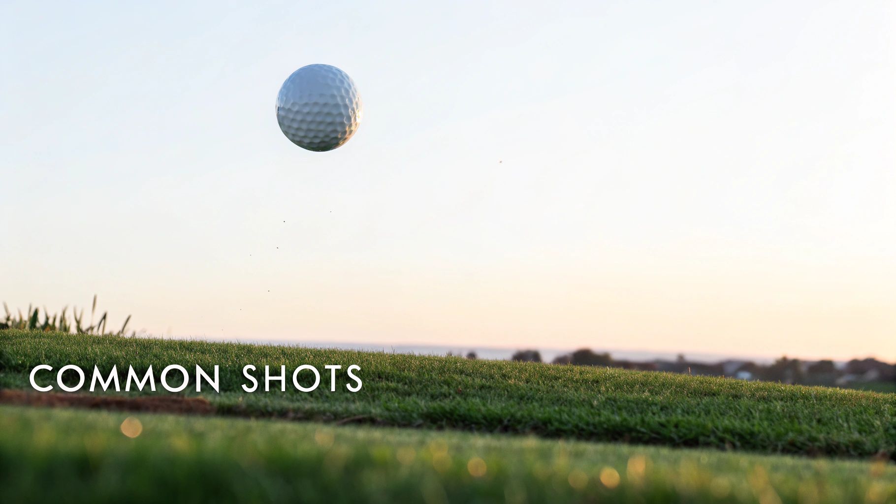 A white golf ball flying high against a clear sky over a vibrant green golf course.