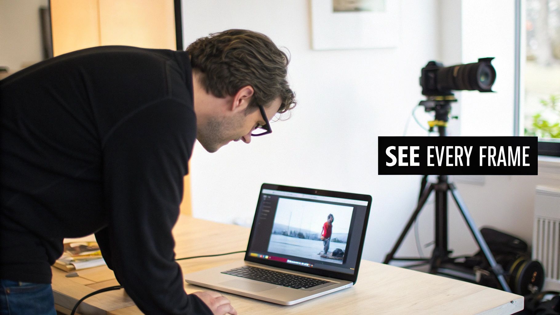 Photographer reviewing frame by frame video footage on laptop with camera on tripod in studio