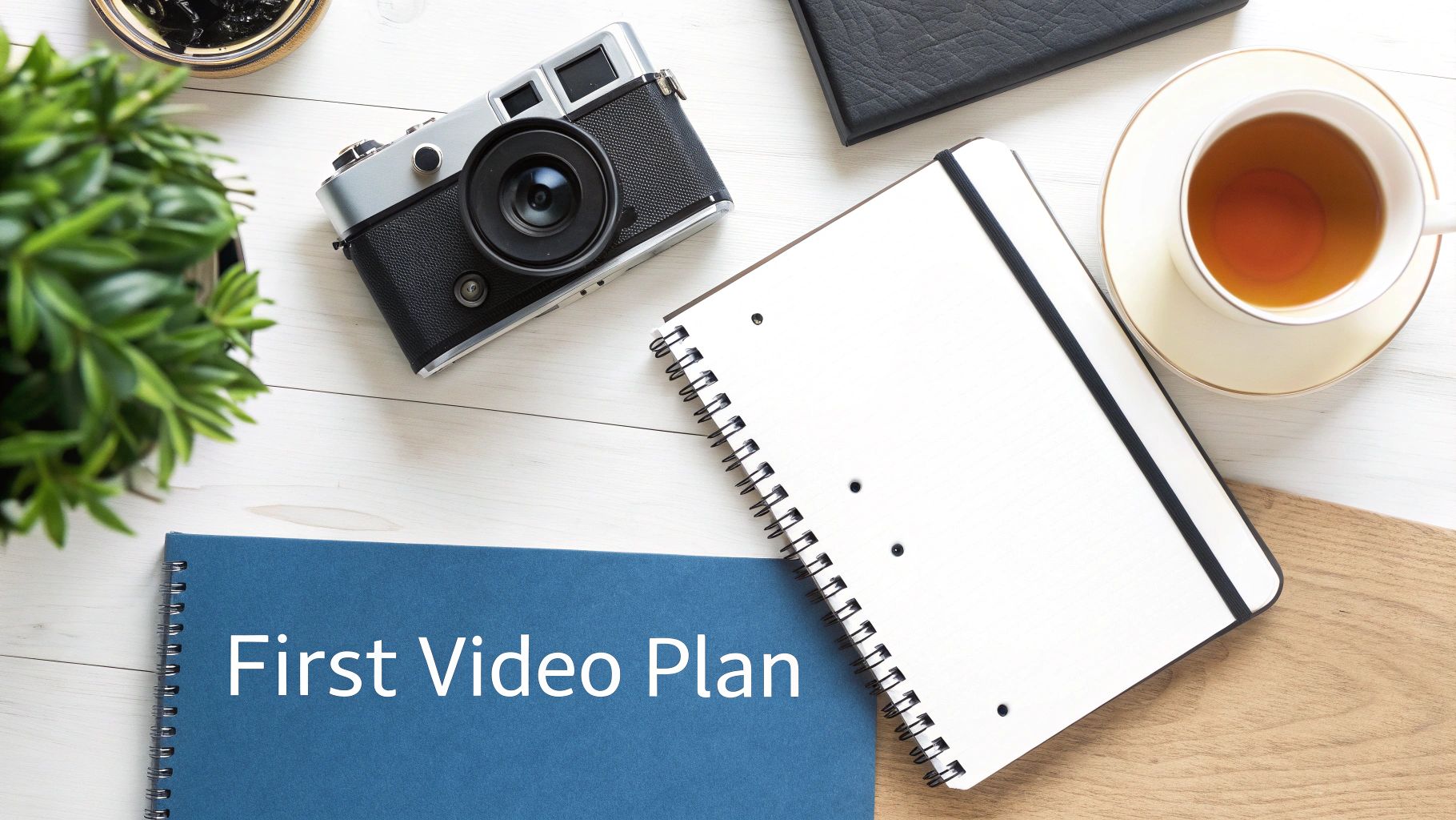 A flat lay of a desk with a notebook titled 'First Video Plan', a camera, and a cup of tea.
