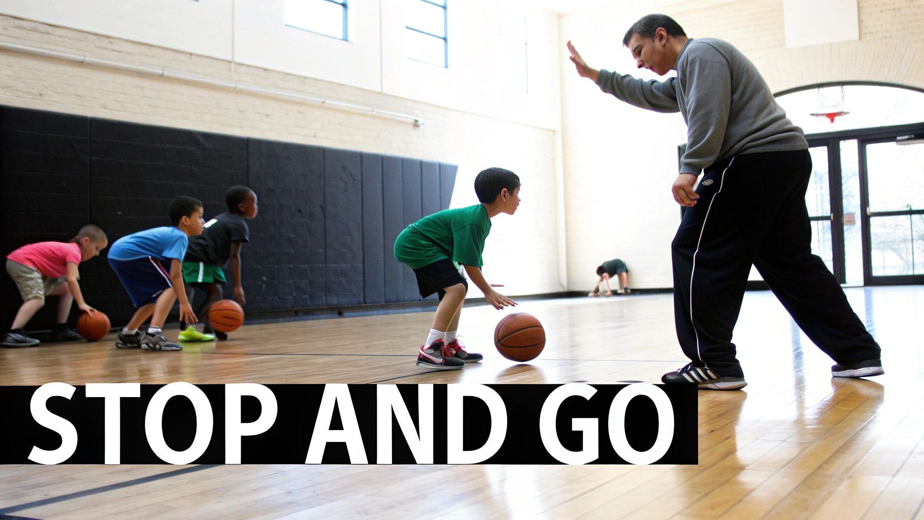 An adult coach guides young boys in a basketball dribbling drill on a gym court.
