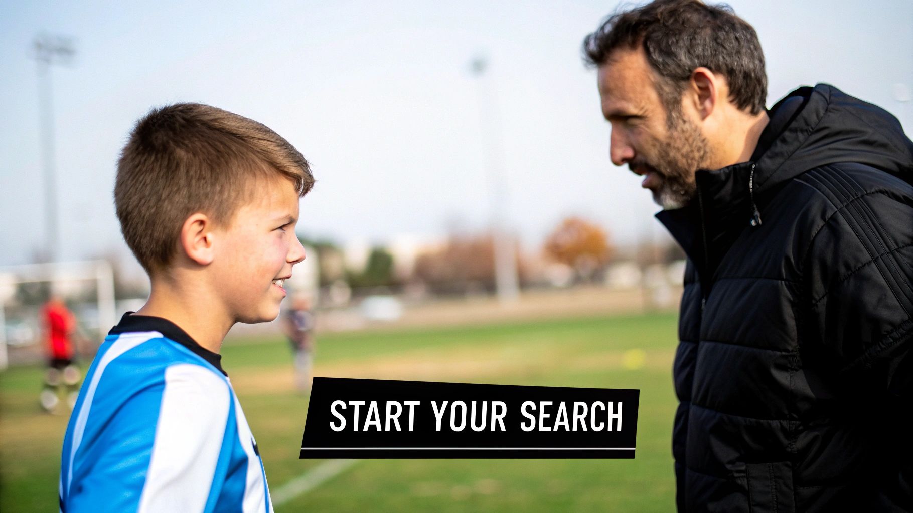 A young boy in a blue soccer uniform smiling at his coach on a green field.