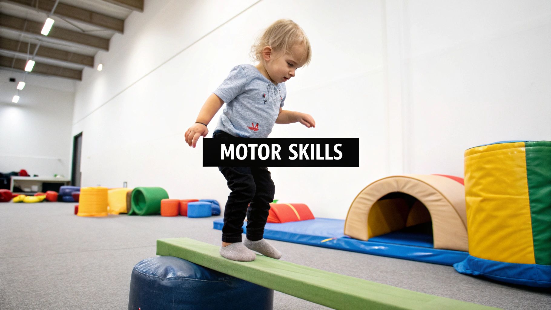 A young child practices balancing on a green beam in an indoor play area, enhancing motor skills.