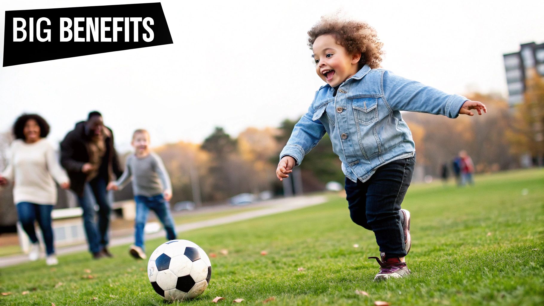A happy toddler with curly hair joyfully kicks a soccer ball on a green field with family.