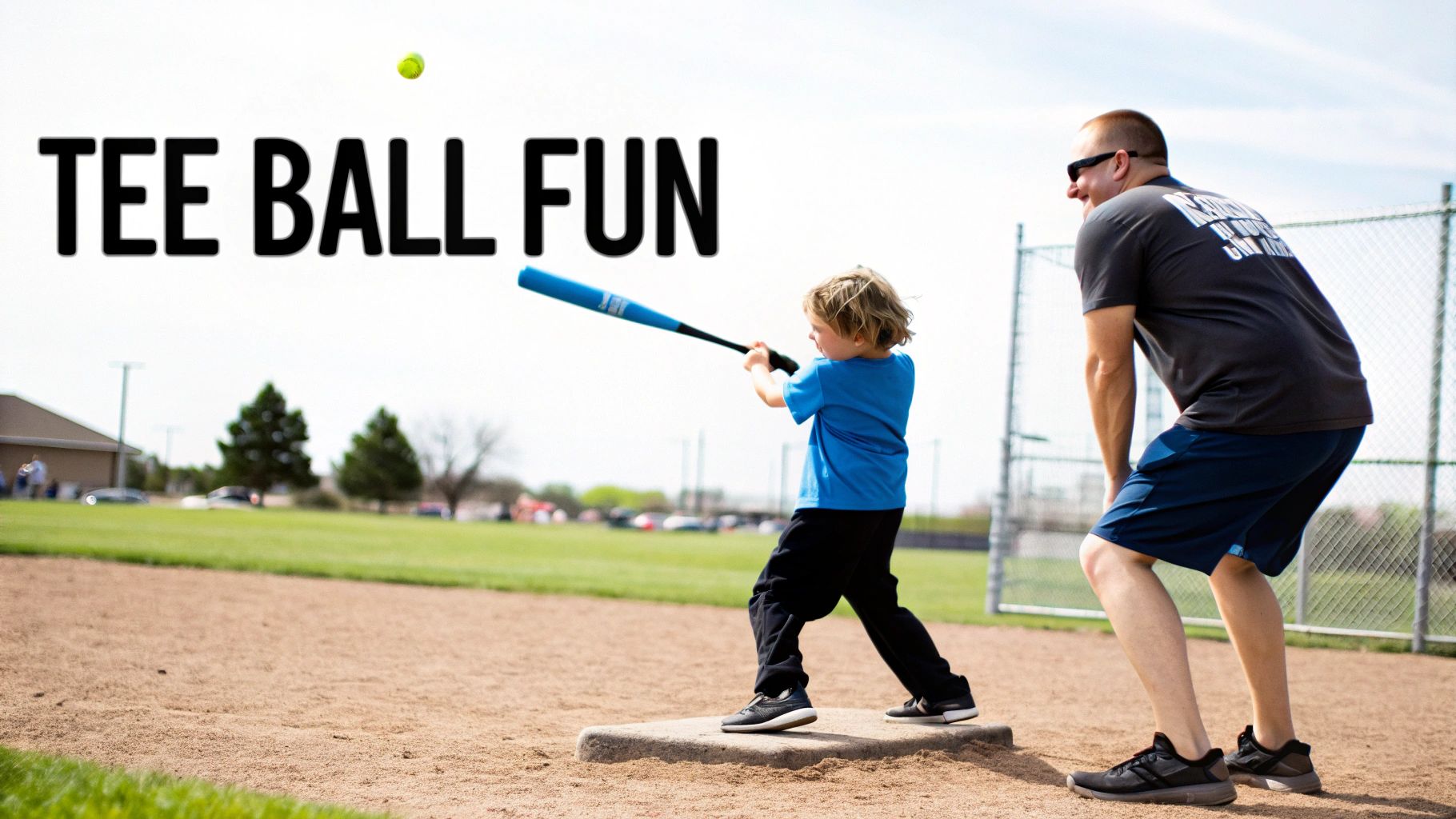 A young child swings a blue baseball bat on a tee-ball field with an adult watching, and a ball in the air.