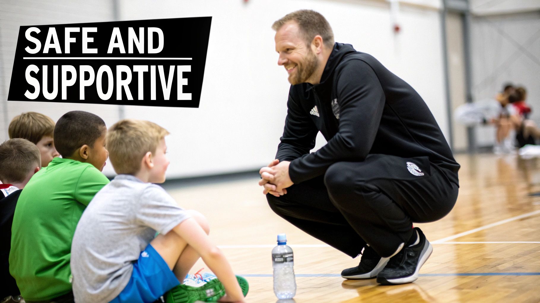 A smiling basketball coach squats on a court, talking to a group of young boys, creating a safe and supportive environment.