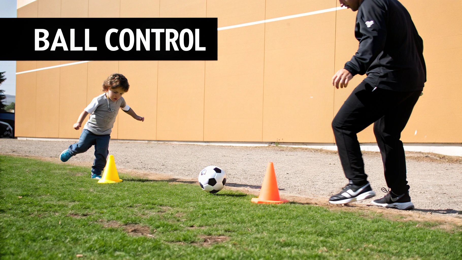 A toddler practices ball control with a soccer ball and cones, supervised by an adult coach.