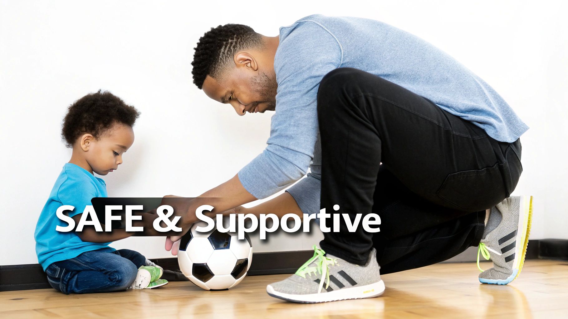 A man and a toddler on the floor interacting with a soccer ball, highlighting a safe and supportive environment.