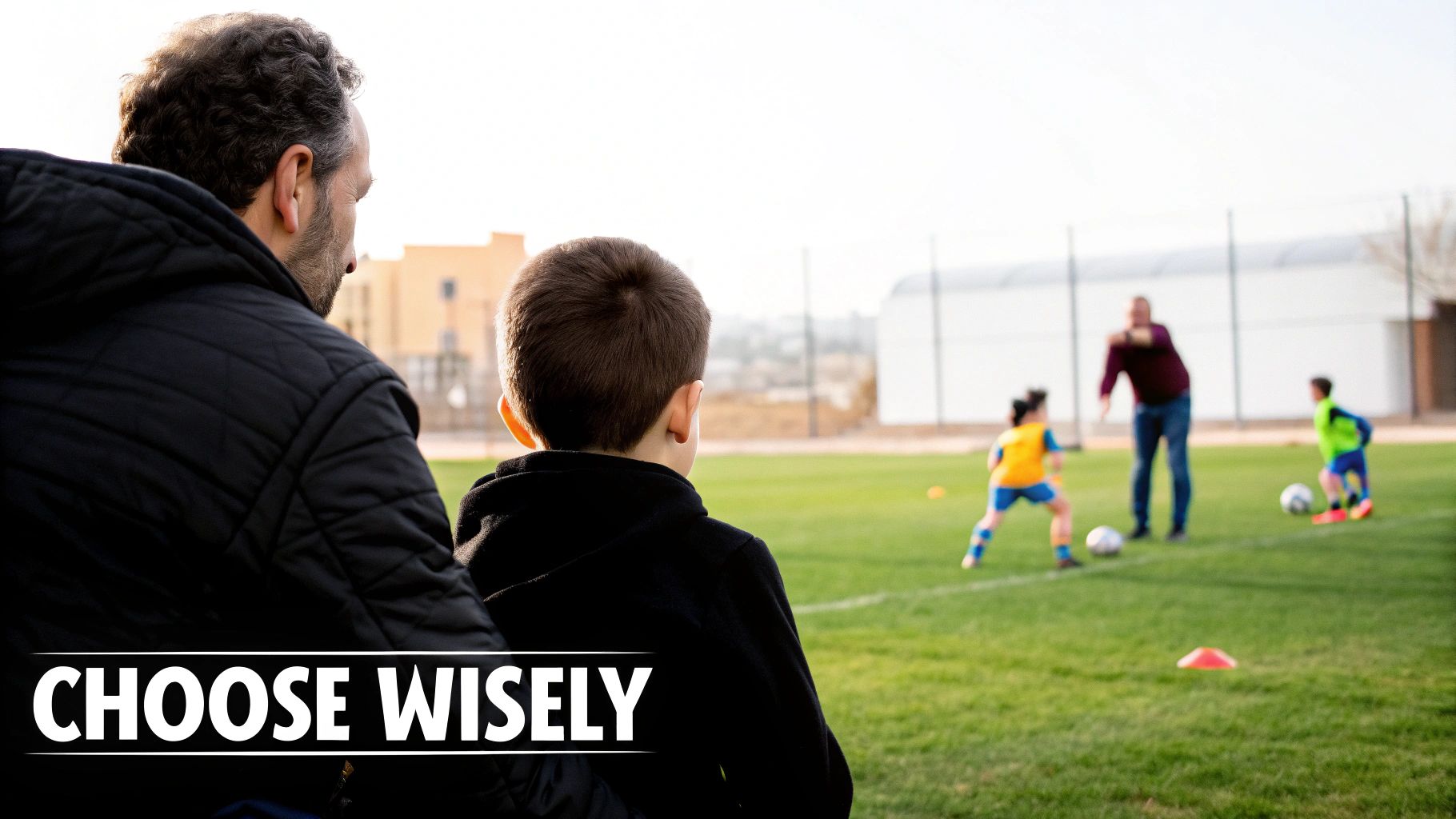 A father and son watch a youth soccer practice with a coach and kids on a green field.