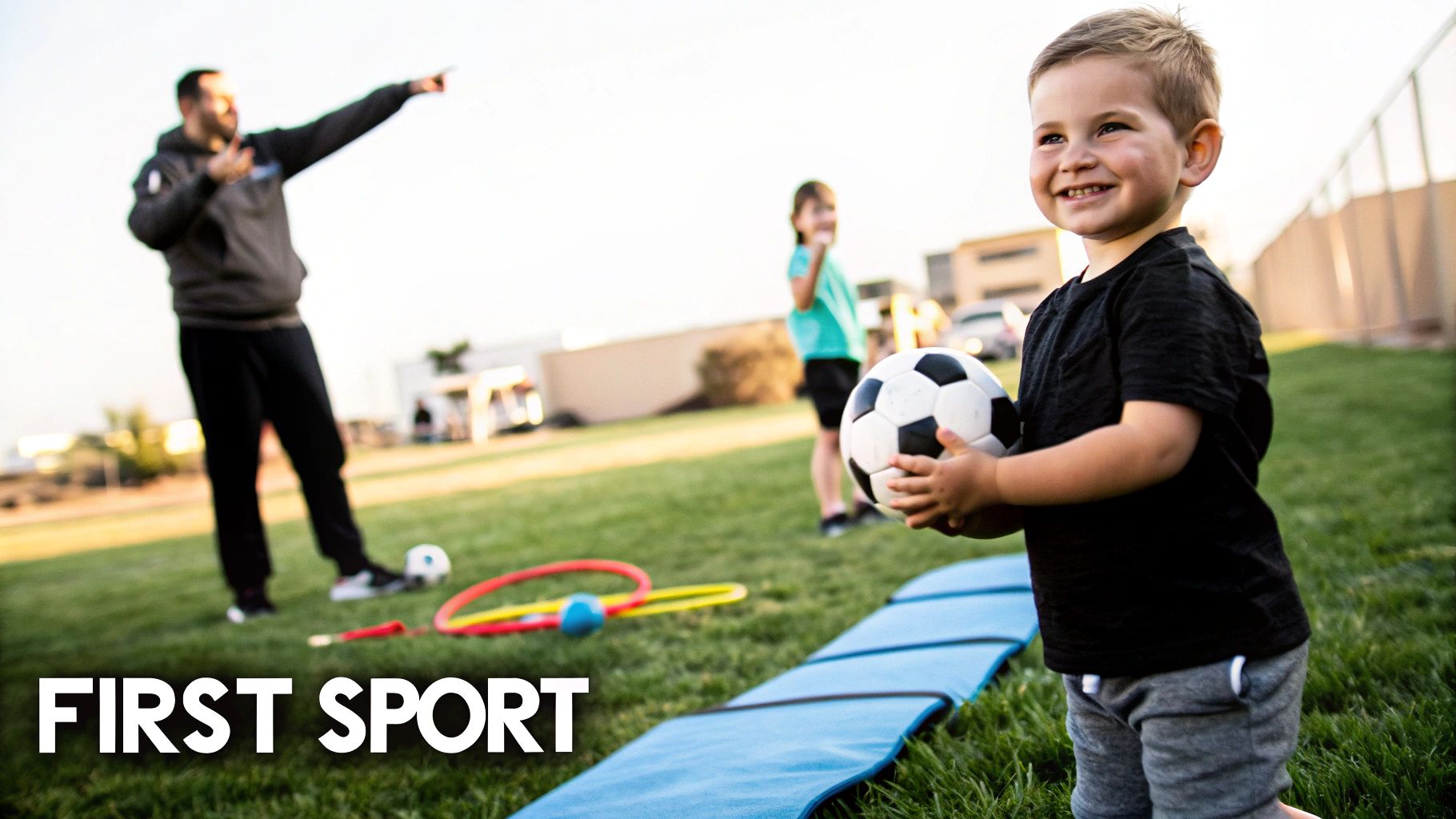 Happy young boy smiles, holding a soccer ball on a grassy field with a coach and child.