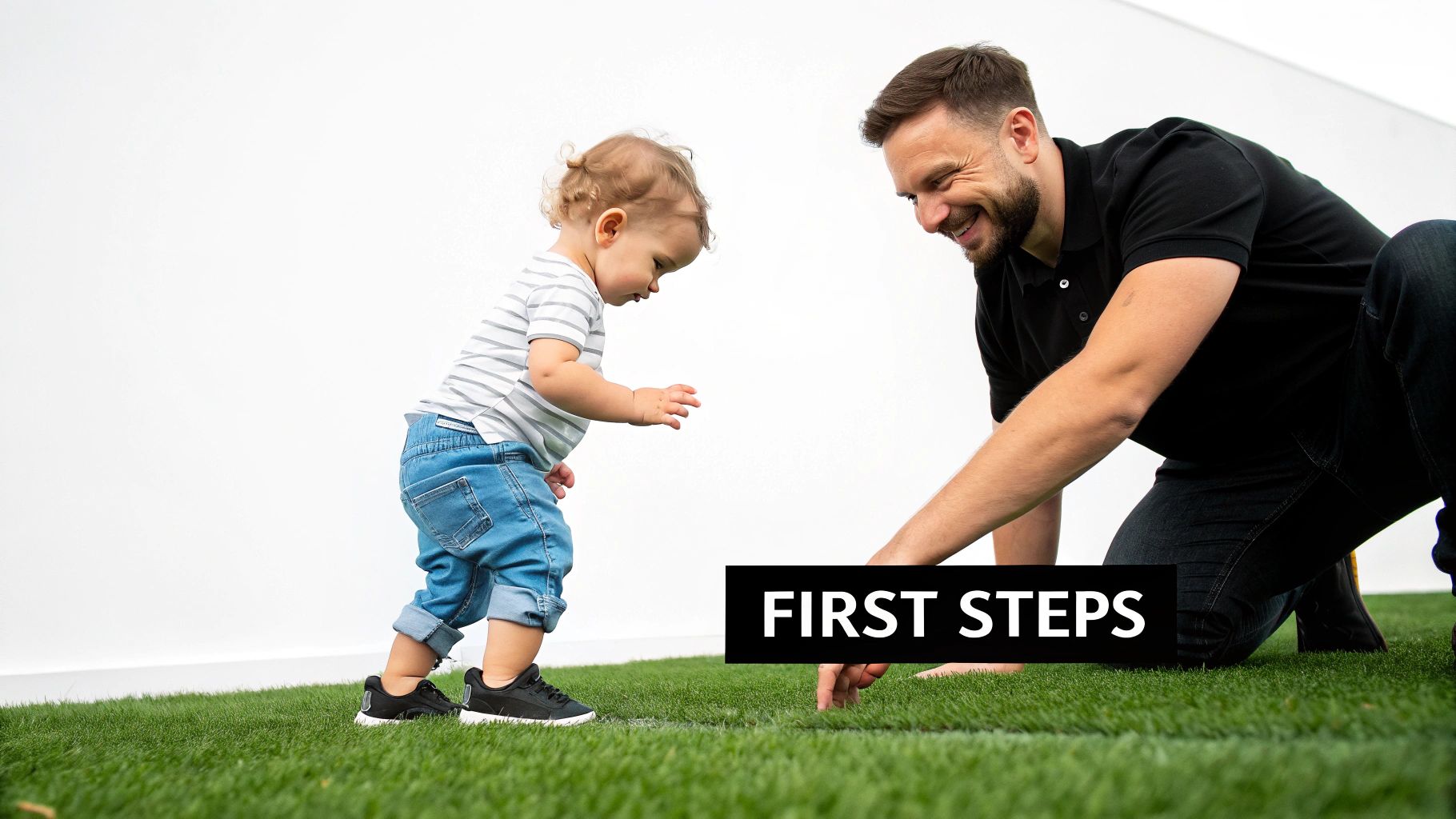 A smiling father watches his young toddler take first steps on green grass.