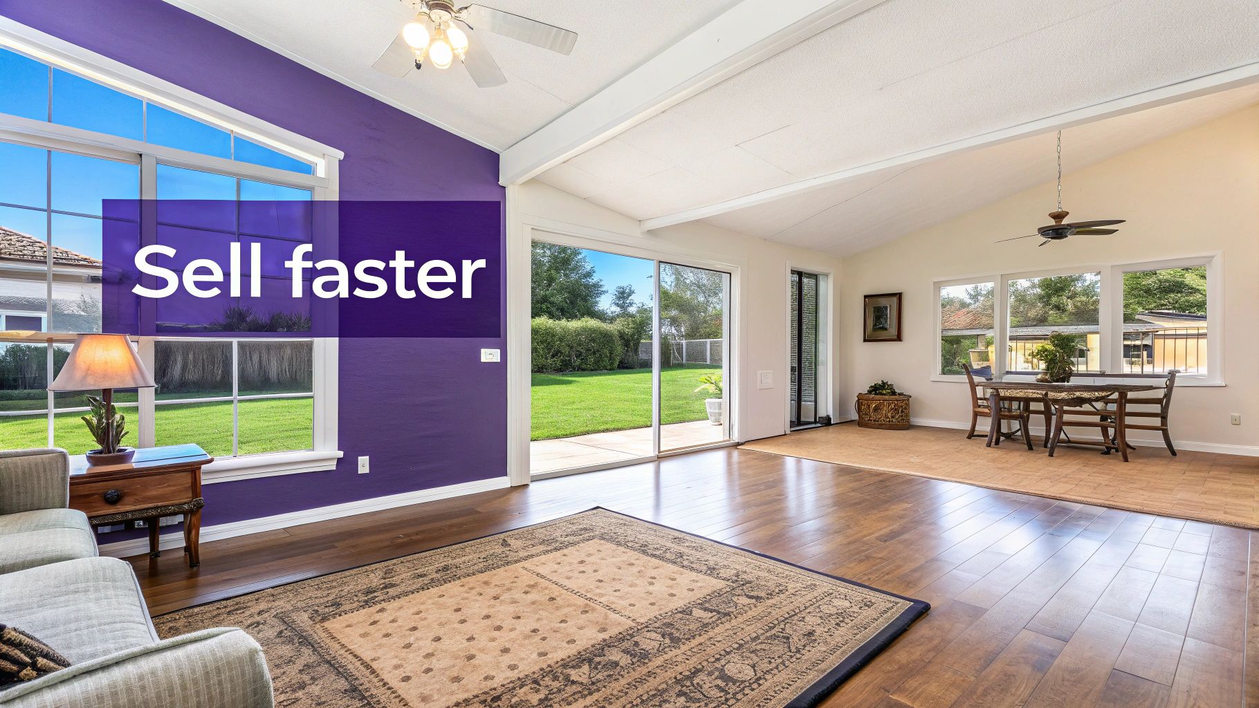 A brightly lit house interior featuring a living room, dining area, hardwood floors, purple wall, and a view of a green backyard.