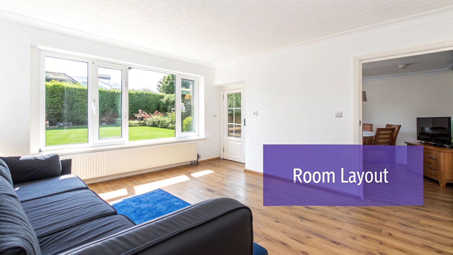 Bright living room with a dark sofa, large windows viewing a green garden, and wooden flooring.