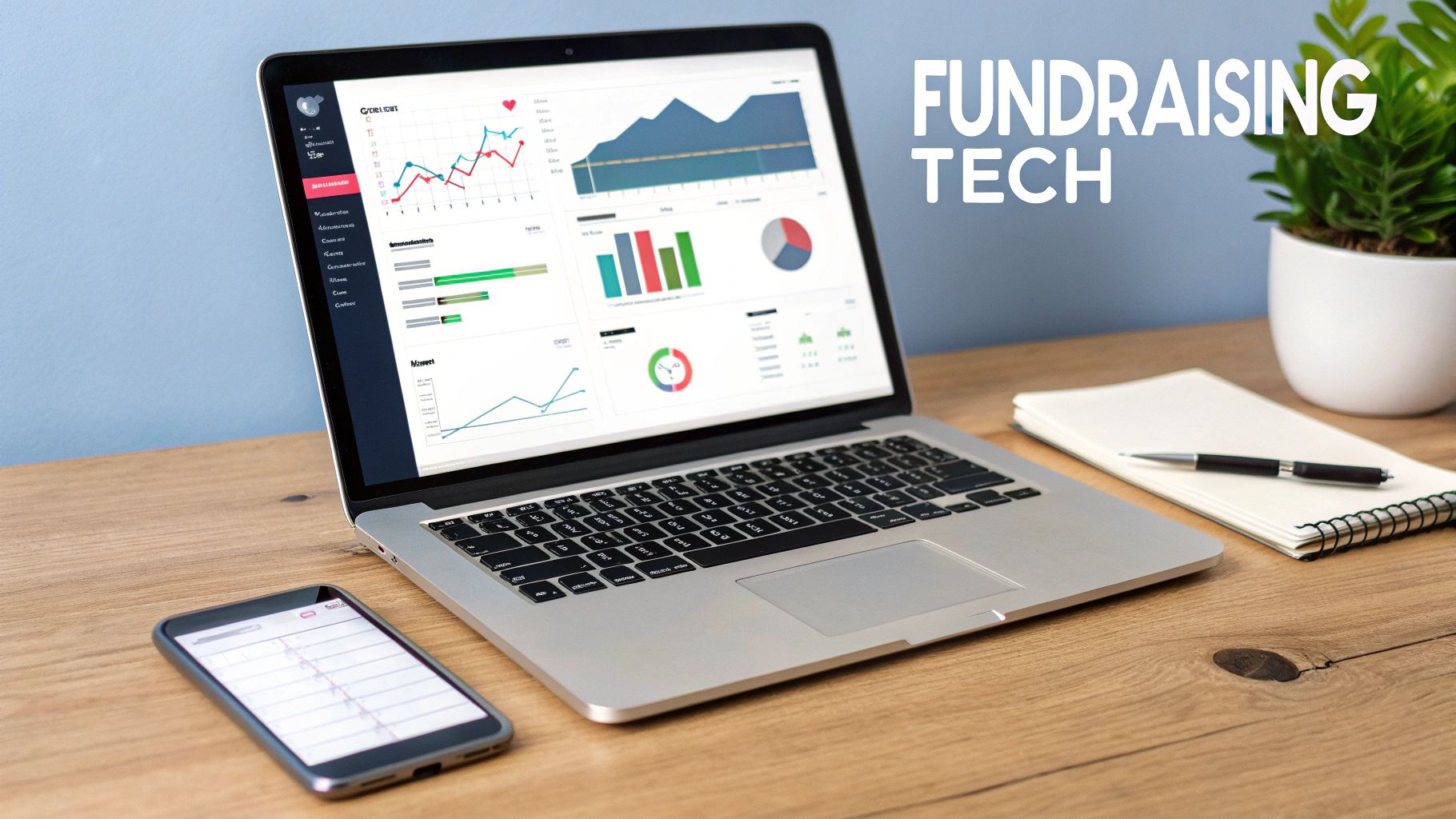 A laptop displaying fundraising analytics, with a smartphone, notebook, pen, and plant on a wooden desk.