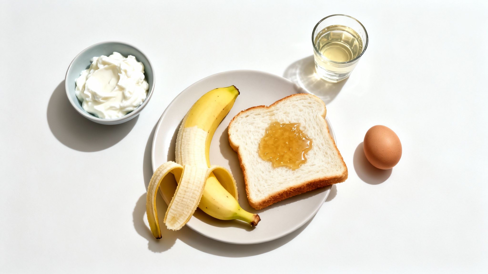 A healthy breakfast spread with a banana, toast with jam, yogurt, egg, and a glass of water.