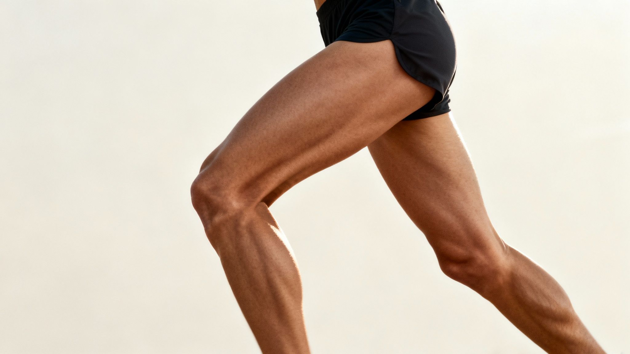 Running legs in black shorts against a light background, showing defined muscles in motion, conveying strength and dynamism.