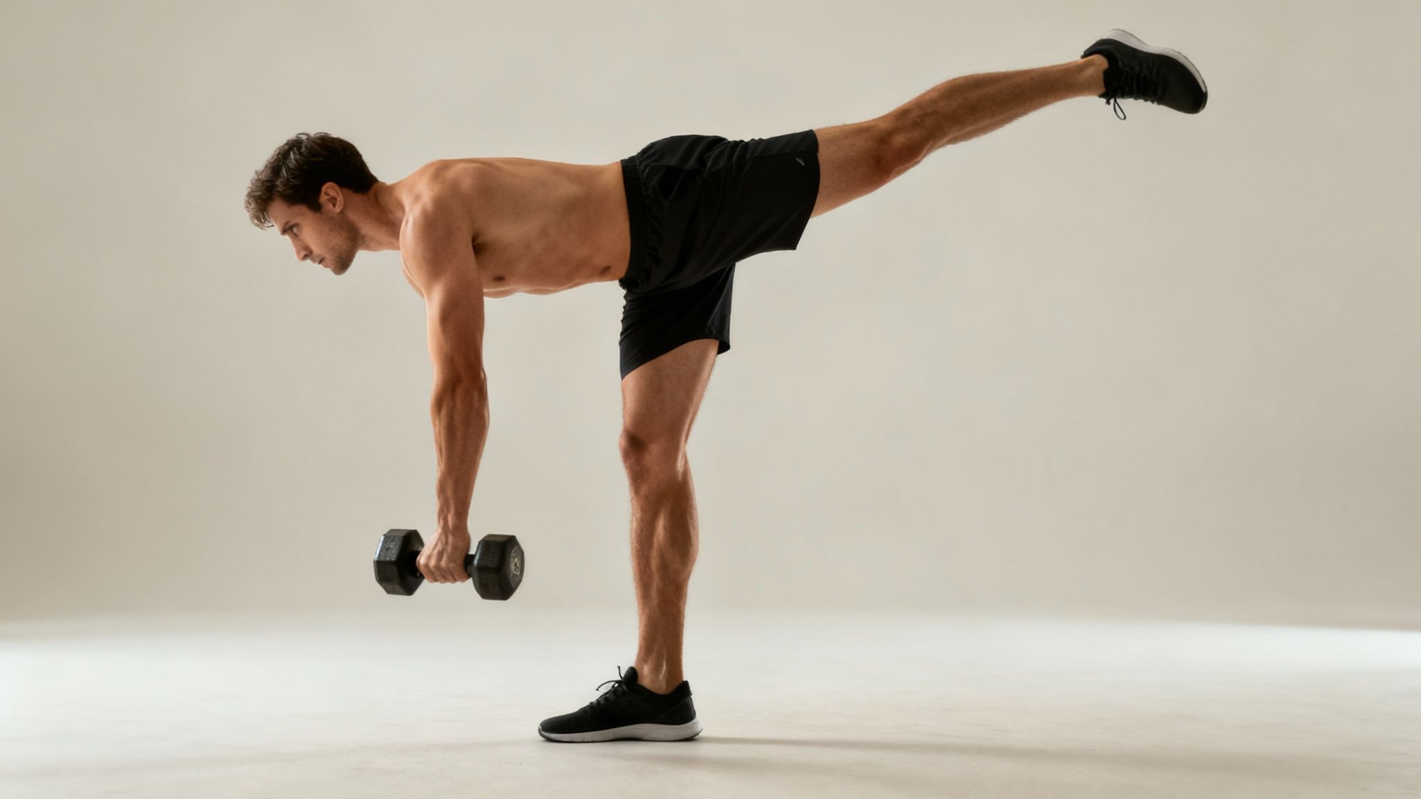 A fit man performs a single-leg dumbbell Romanian deadlift, balancing on one leg, focused on hamstring exercise.
