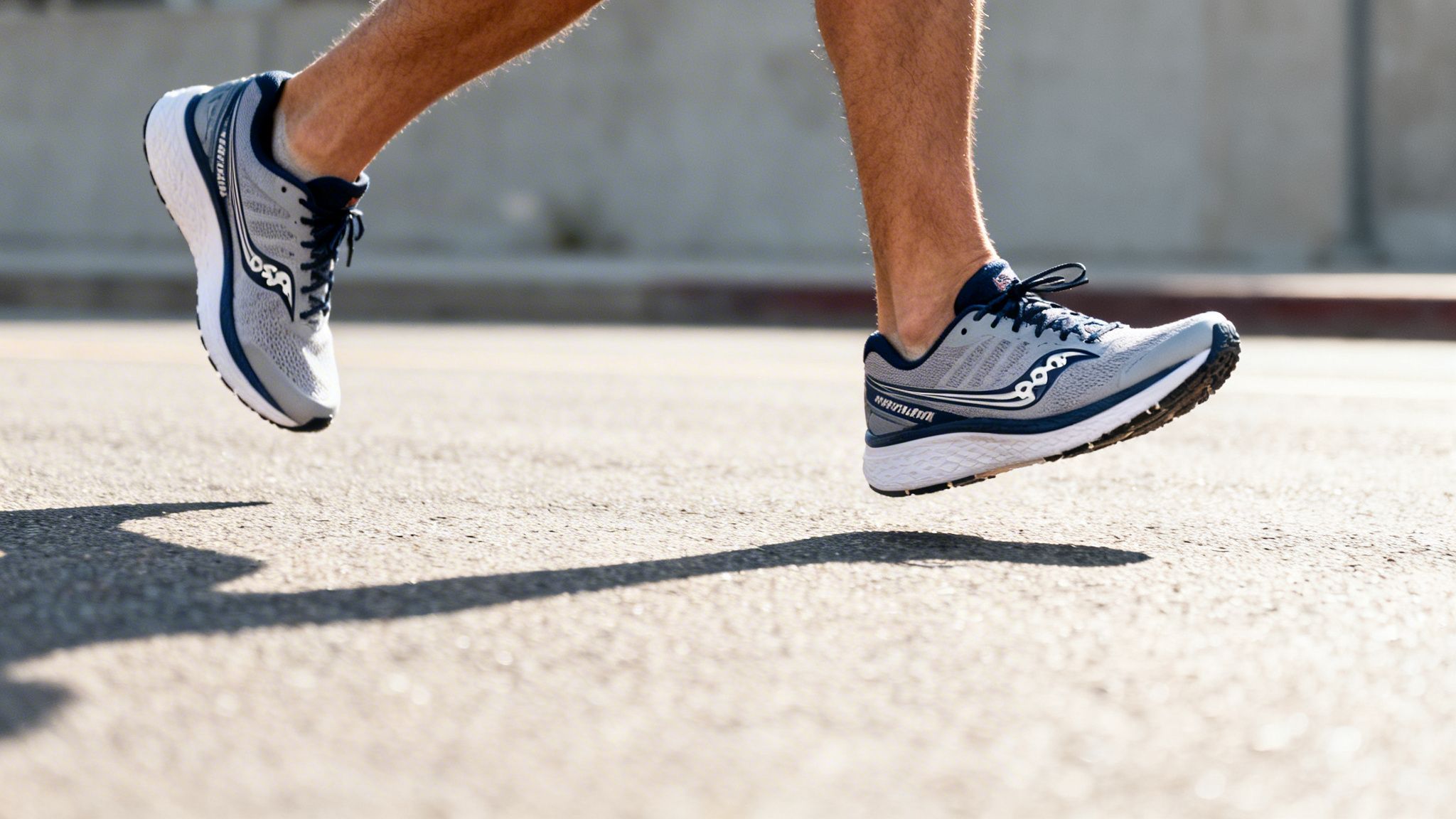 Close-up of a person running in blue and grey sneakers on a sunlit road. The shadow is visible on the pavement.