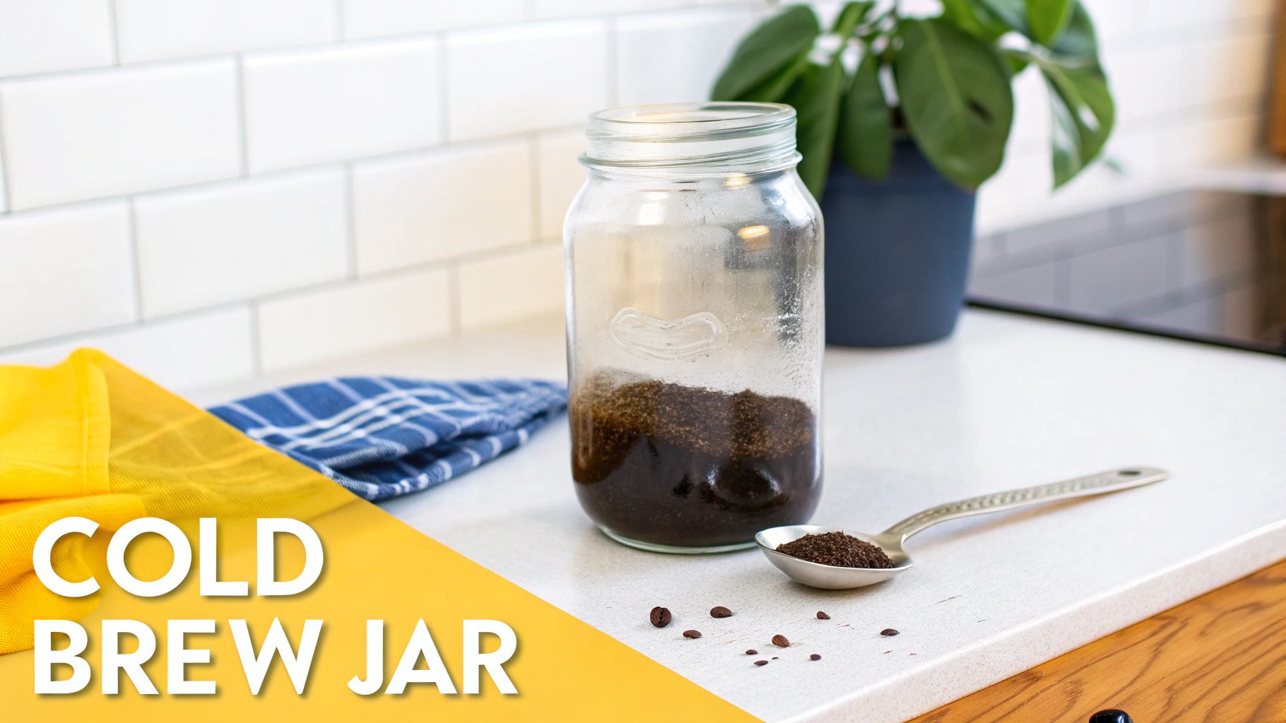 A mason jar on a kitchen counter containing coffee grounds and water for cold brew, with a spoon of grounds nearby.