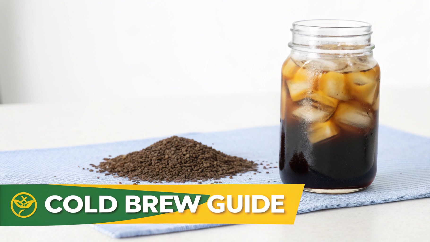 A glass jar of iced cold brew coffee next to a pile of coffee grounds on a blue cloth.