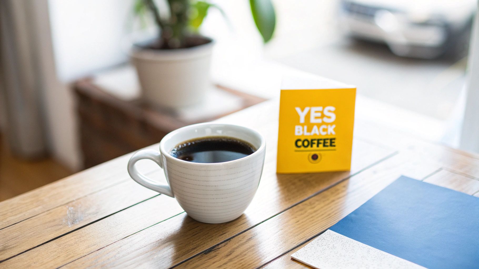 A cup of black coffee and a 'YES BLACK COFFEE' box on a wooden table.