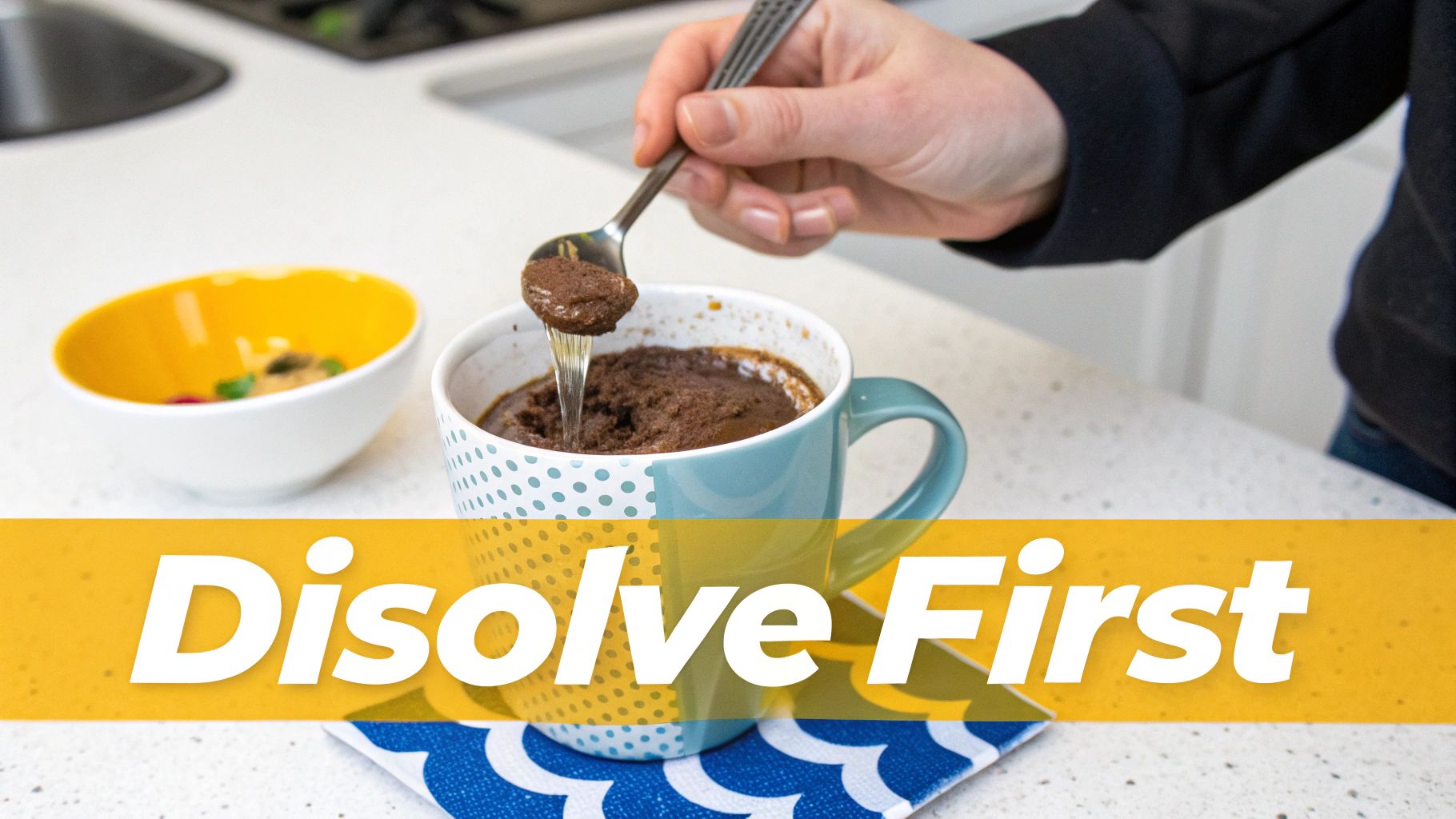 A hand spoons thick chocolate batter into a mug, suggesting a mug cake preparation on a kitchen counter.
