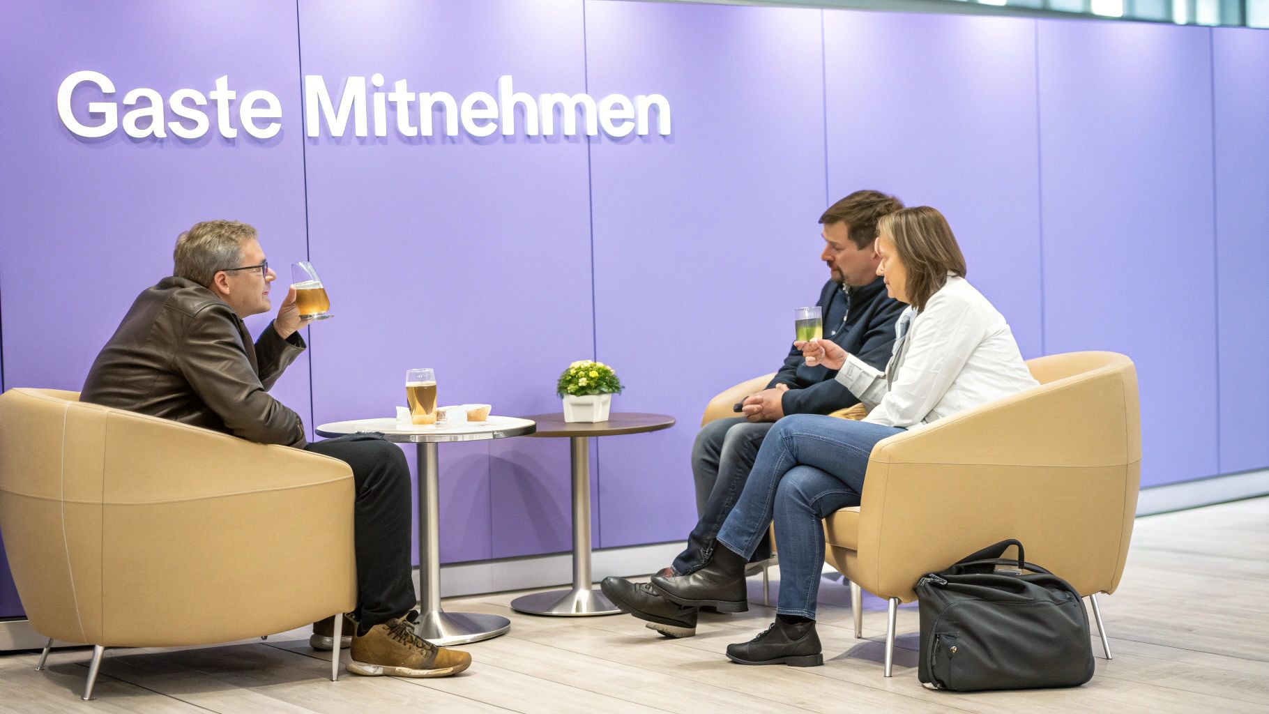 Drei Personen sitzen entspannt in einer Lounge, trinken Getränke und unterhalten sich. Im Hintergrund ein Schild.