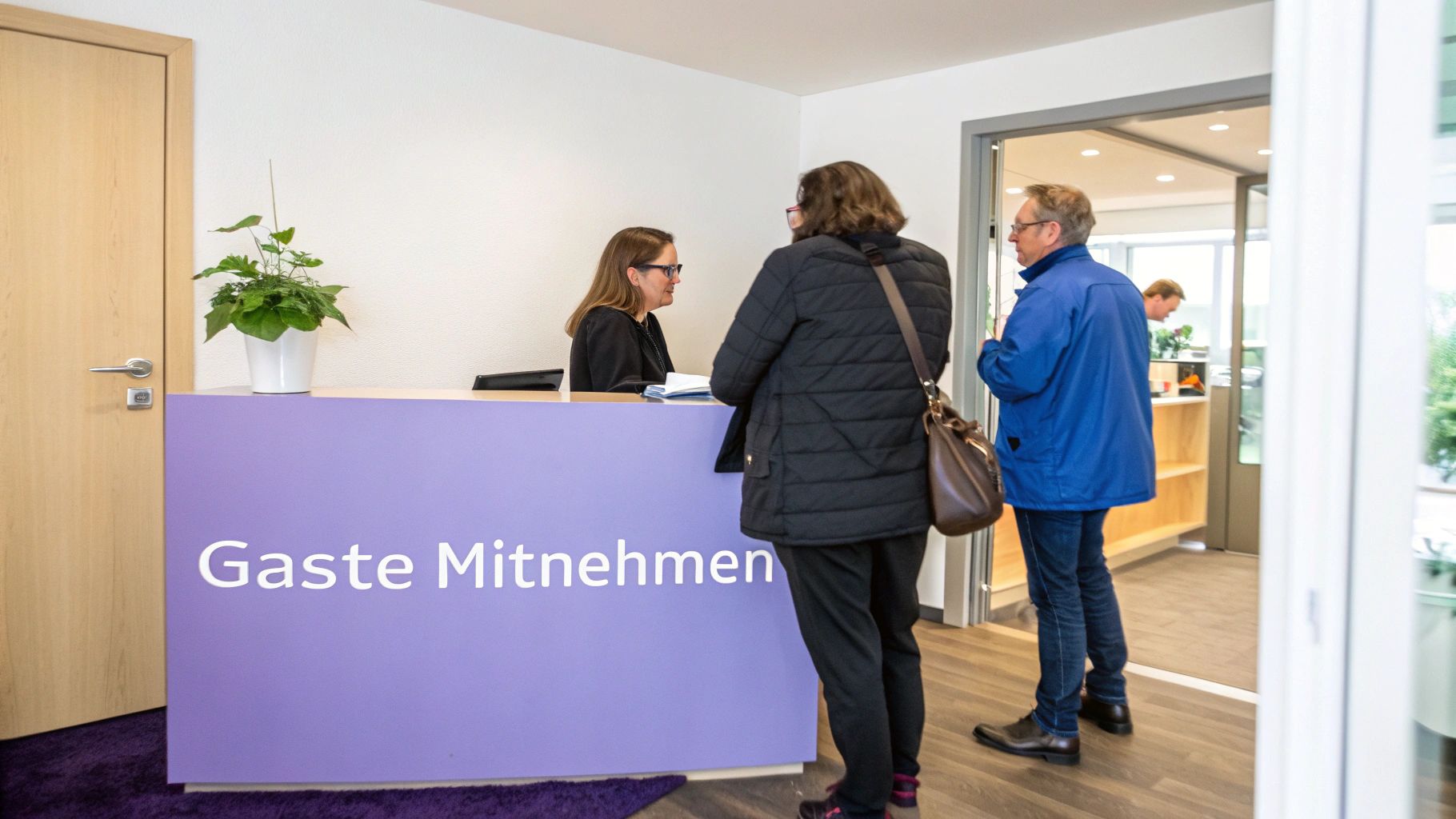 Rezeptionsbereich mit Empfangsdame, die mit zwei wartenden Personen spricht. Ein lila Tresen ist sichtbar.