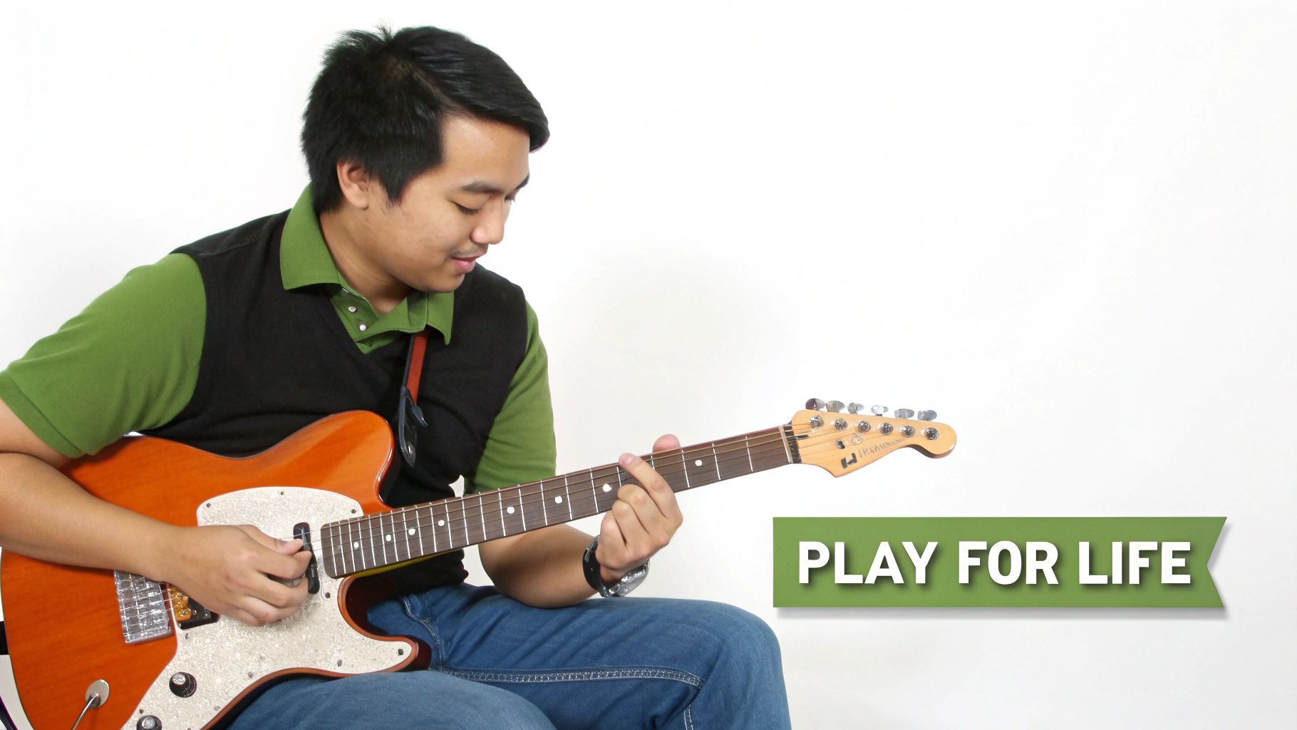 A smiling man sits, focused on playing an orange electric guitar, with the text 'PLAY FOR LIFE'.