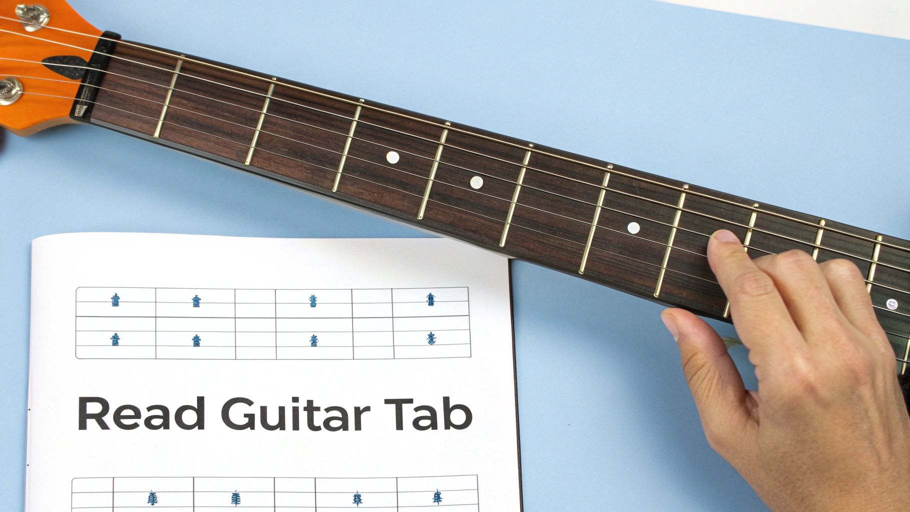 A hand presses a string on a guitar fretboard next to a 'Read Guitar Tab' sheet.