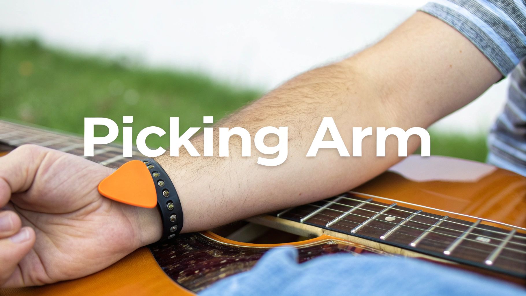 A person's arm rests on an acoustic guitar, with an orange guitar pick tucked under a wristband.