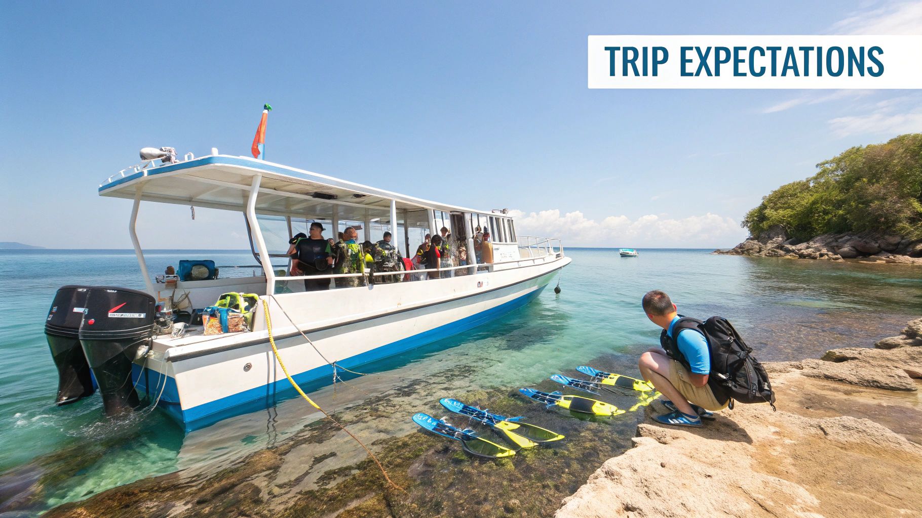 A boat with divers docked at a rocky shore with a man and snorkeling fins in clear water.