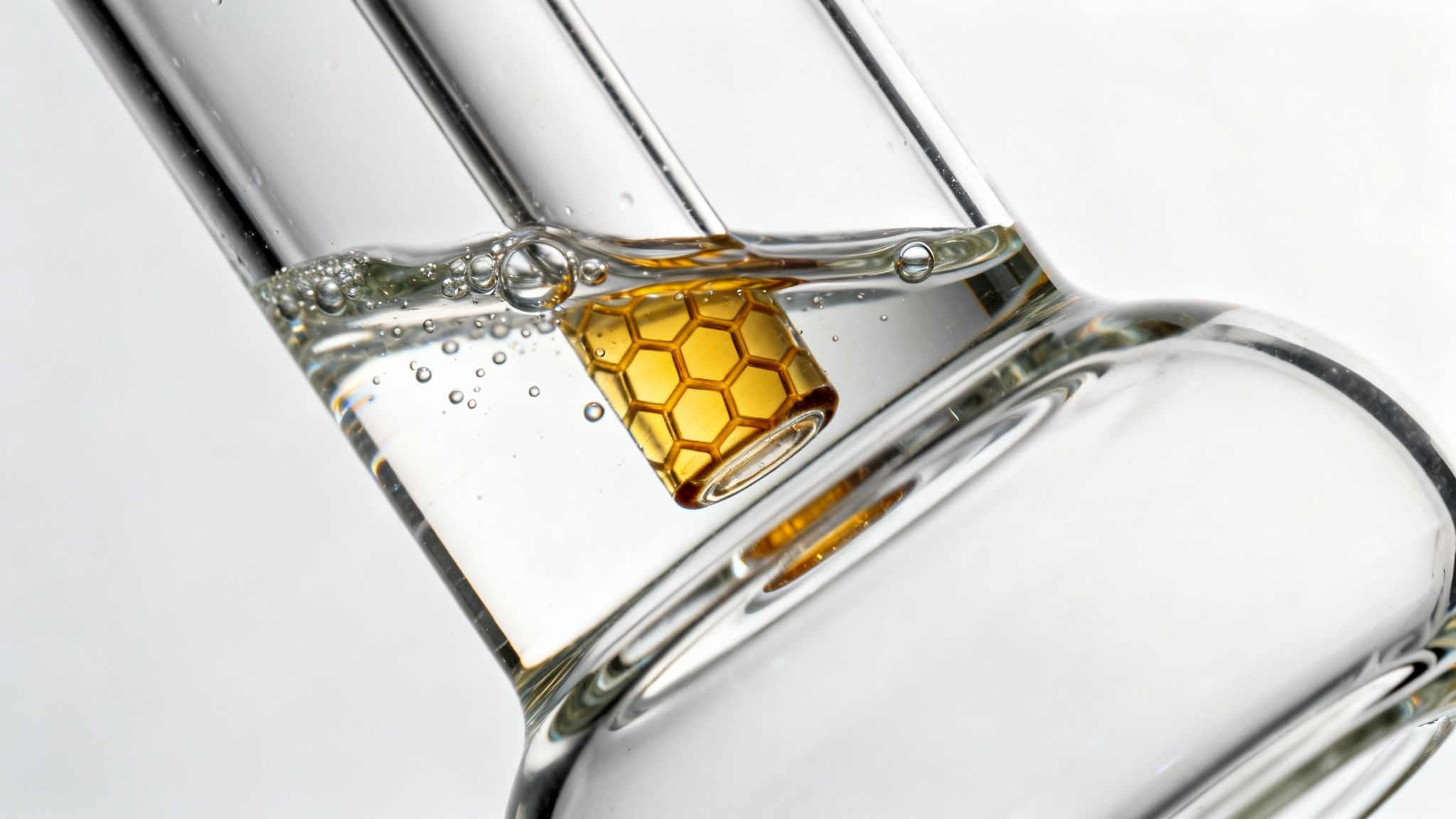 Close-up of a clear glass dab rig with water, bubbles, and a golden honeycomb percolator.