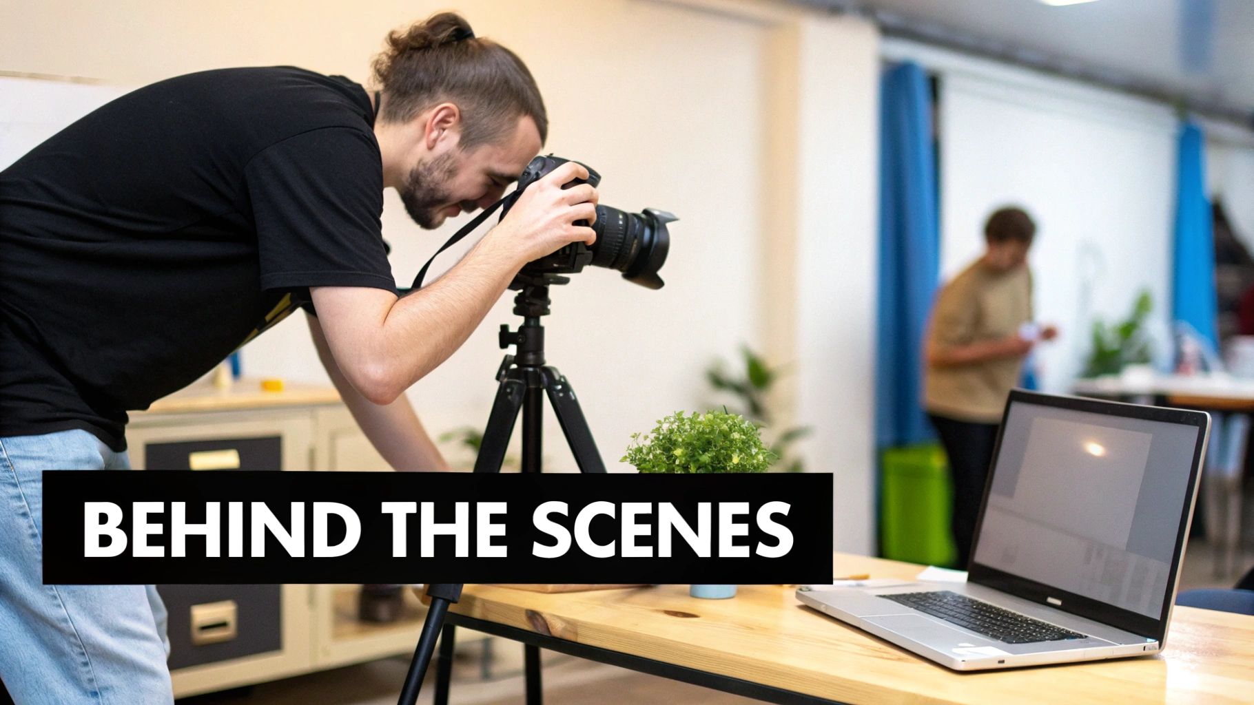 A man with a bun takes a photo with a camera on a tripod, behind the scenes of content creation.