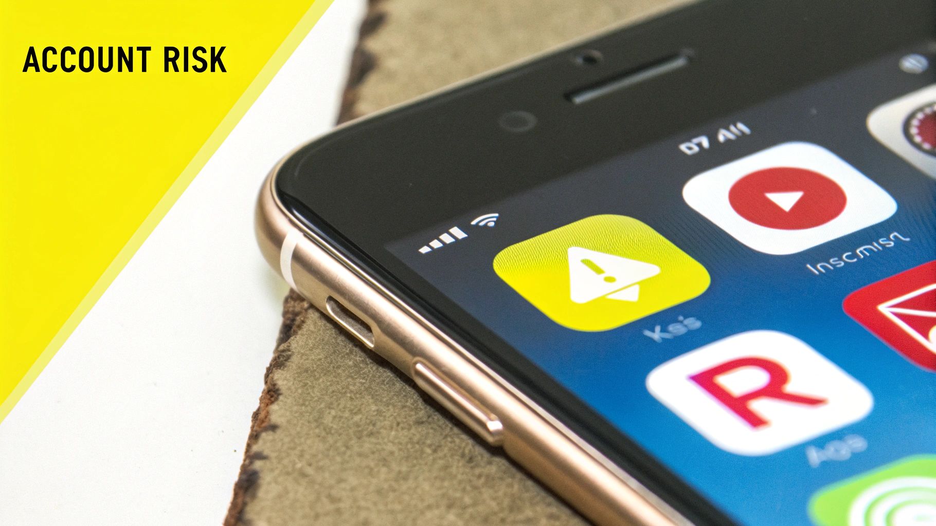 Close-up of a gold smartphone screen showing a warning icon, various apps, and "ACCOUNT RISK" text.