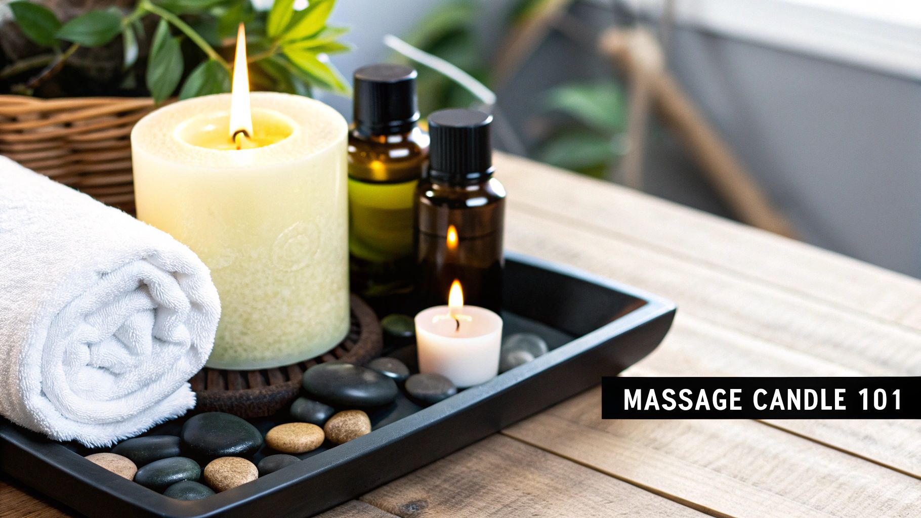 A spa setting with a rolled towel, lit candles, essential oils, and massage stones on a wooden tray.