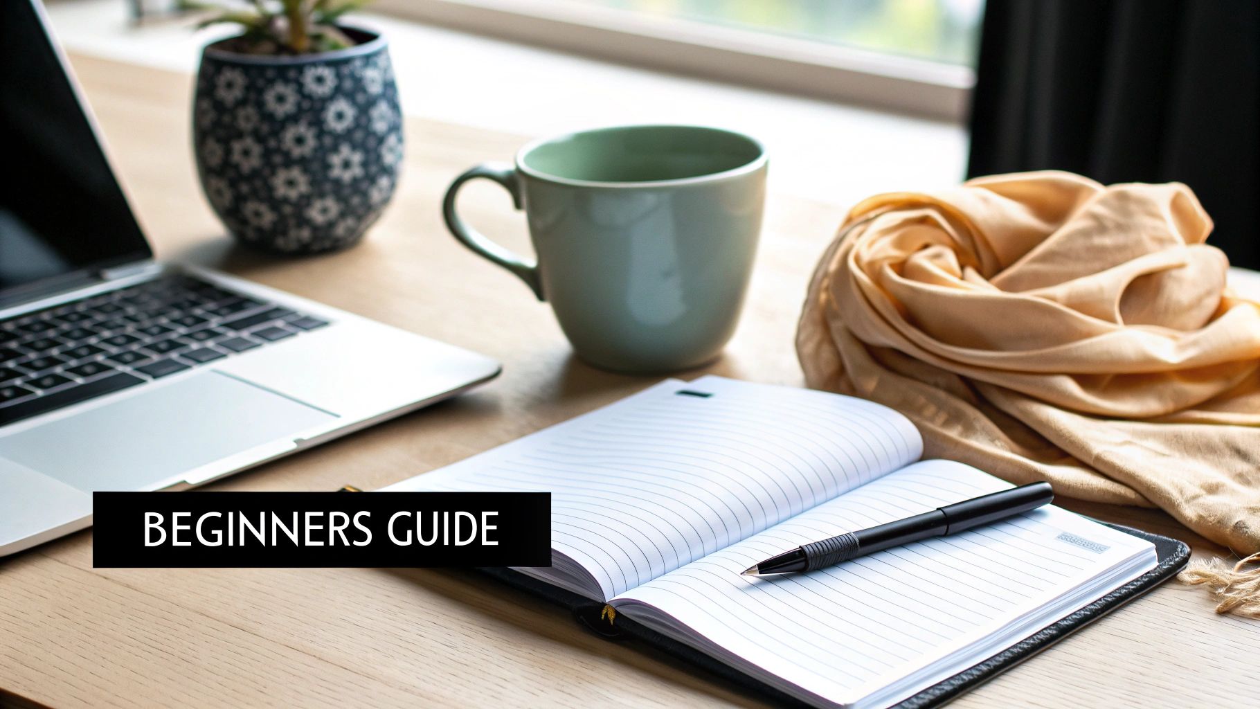 A modern desk setup with a laptop, green mug, open notebook, pen, and plant.
