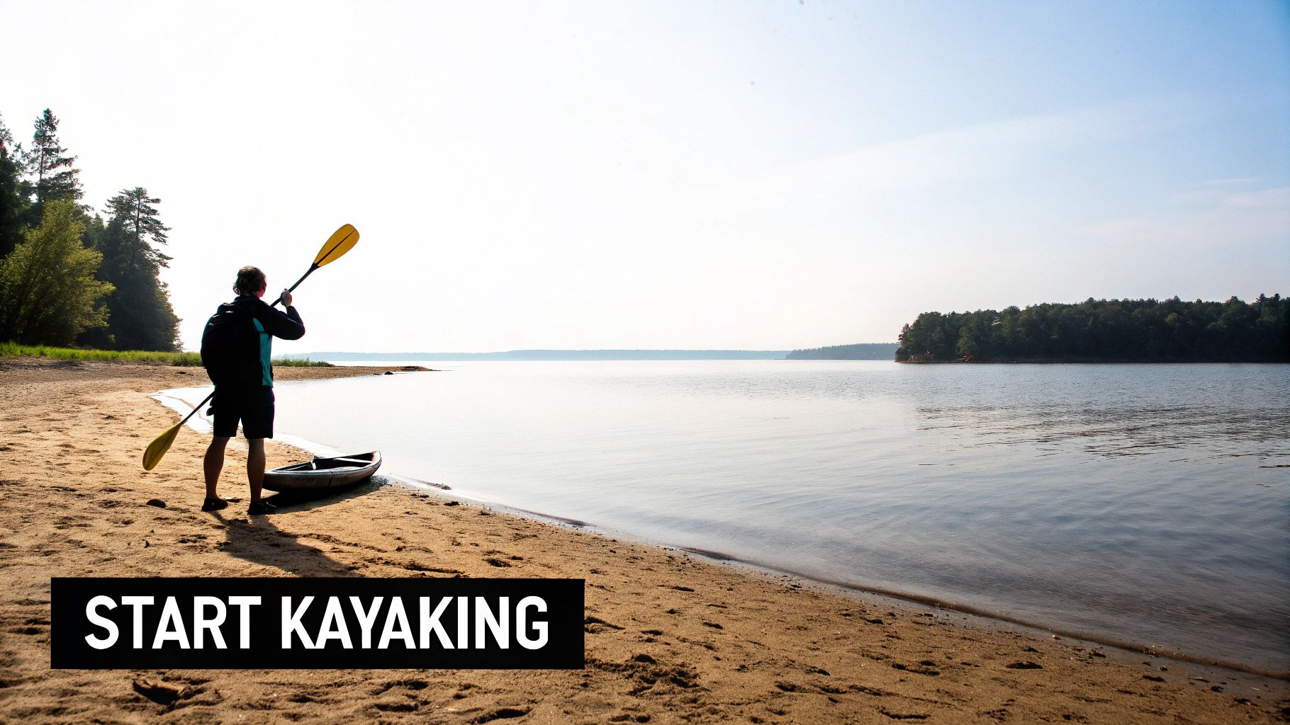 A person stands on a sandy beach with a kayak and paddle, looking at a calm lake.