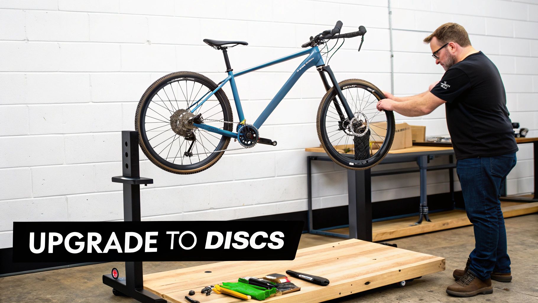 A man upgrades a blue bicycle to disc brakes on a workshop stand.