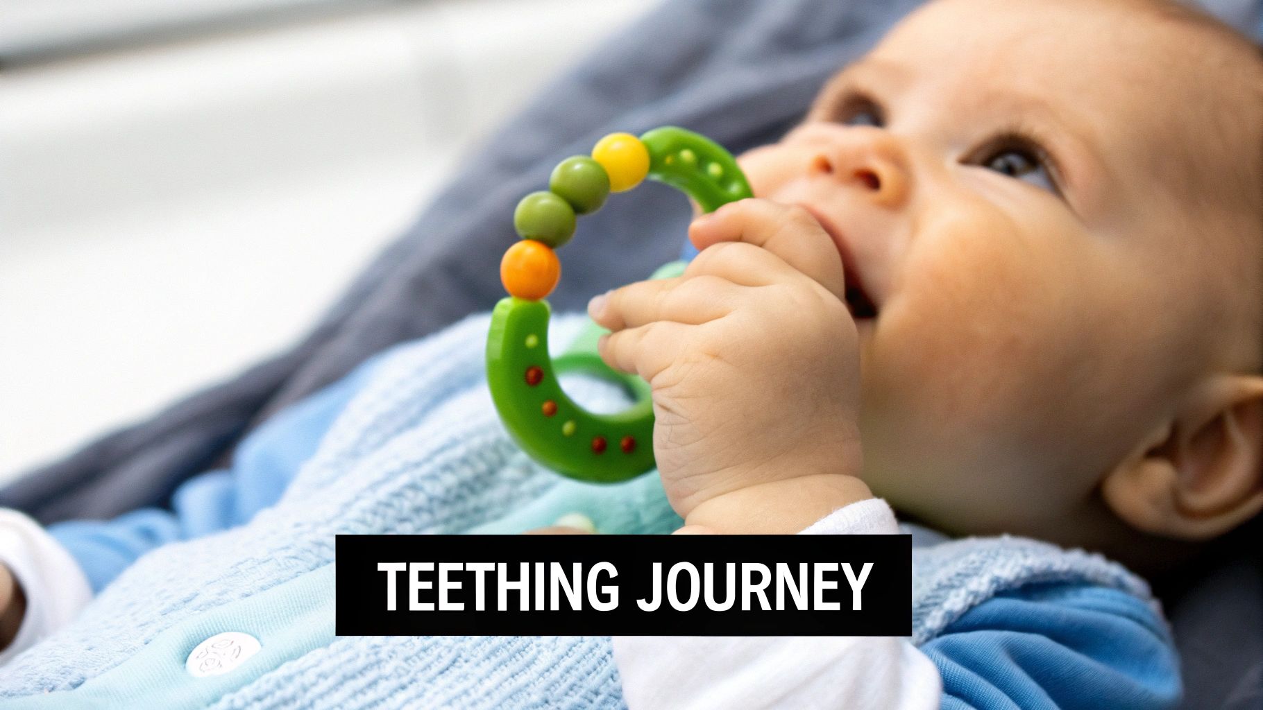 A cute baby with rosy cheeks holds a green and colorful teether, lying comfortably on a blanket.