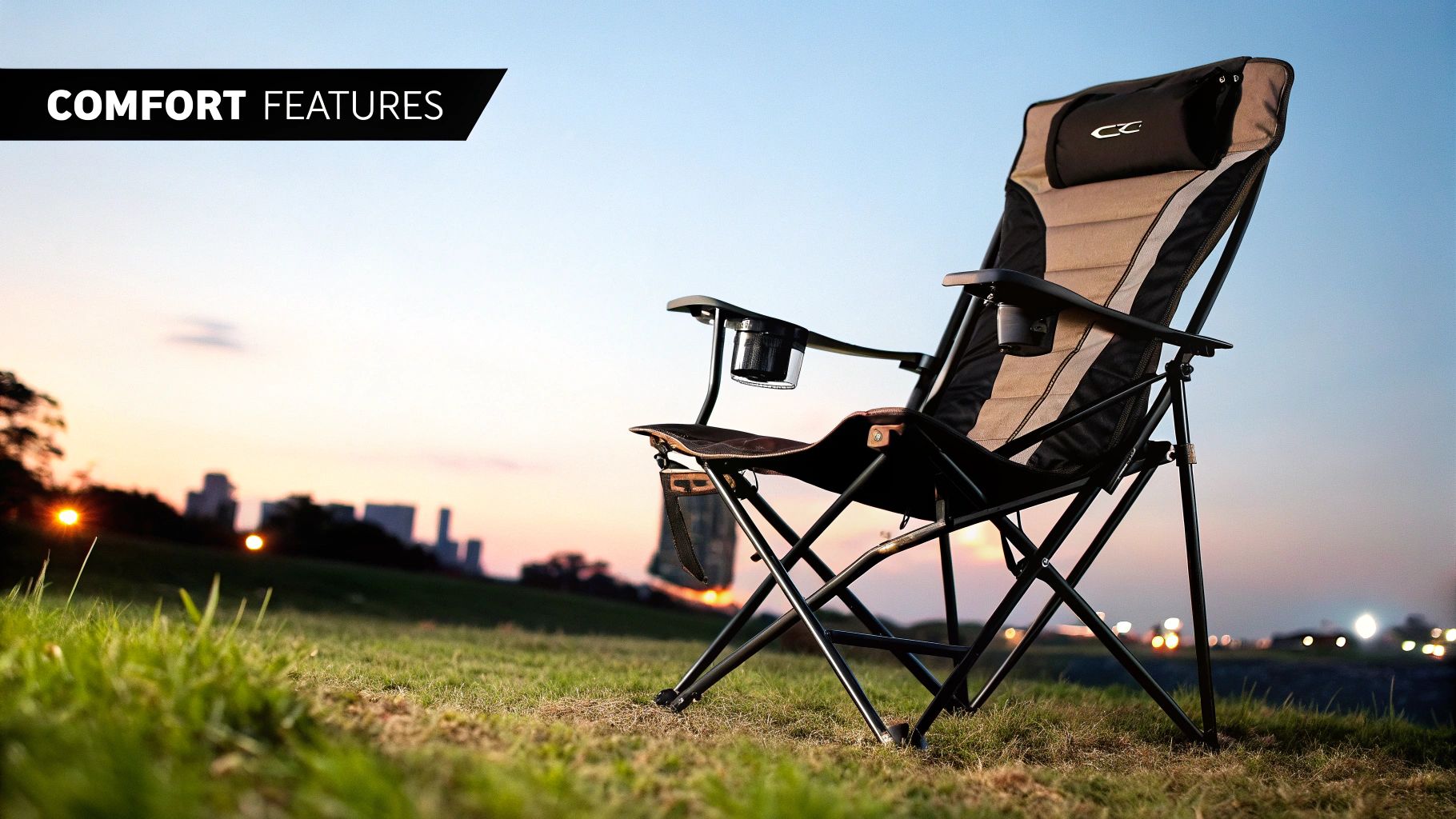 A comfortable black and tan folding camping chair with cup holders on a grassy hill at sunset.