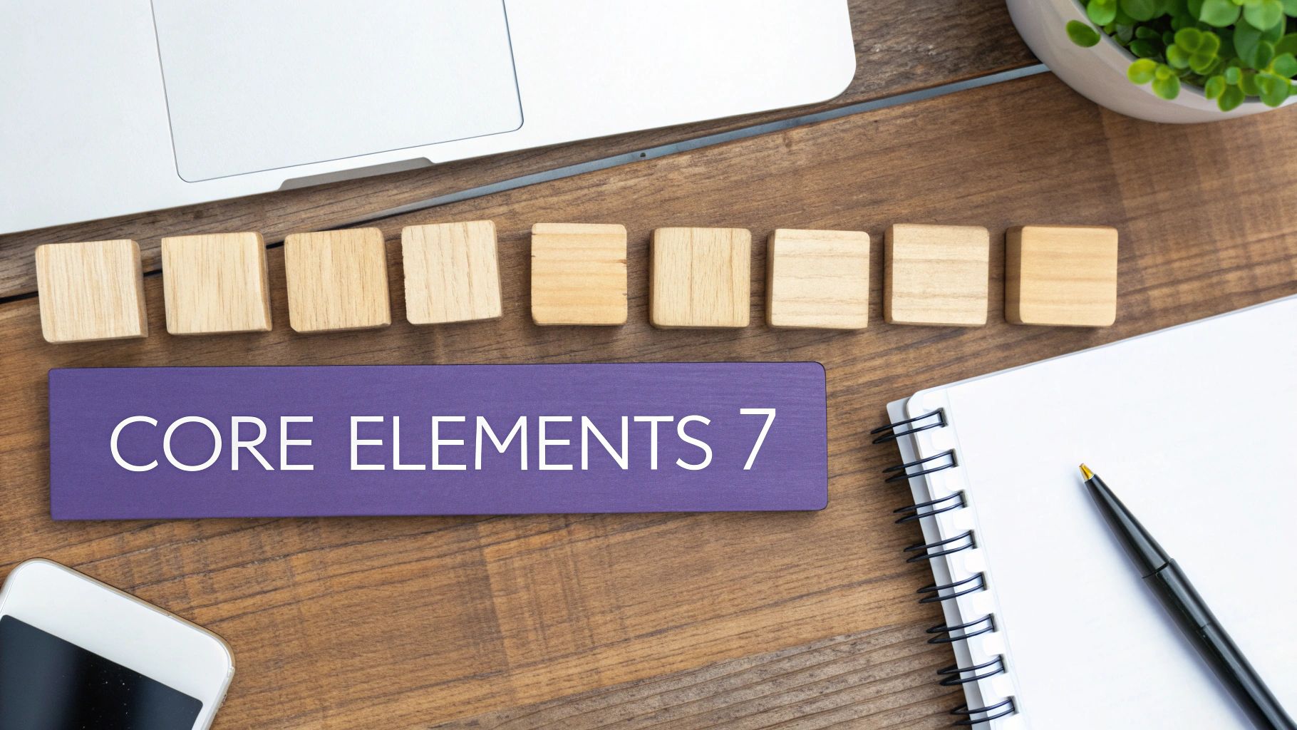 Flat lay of a desk with a laptop, wooden blocks, a sign reading 'CORE ELEMENTS 7', and a notebook.