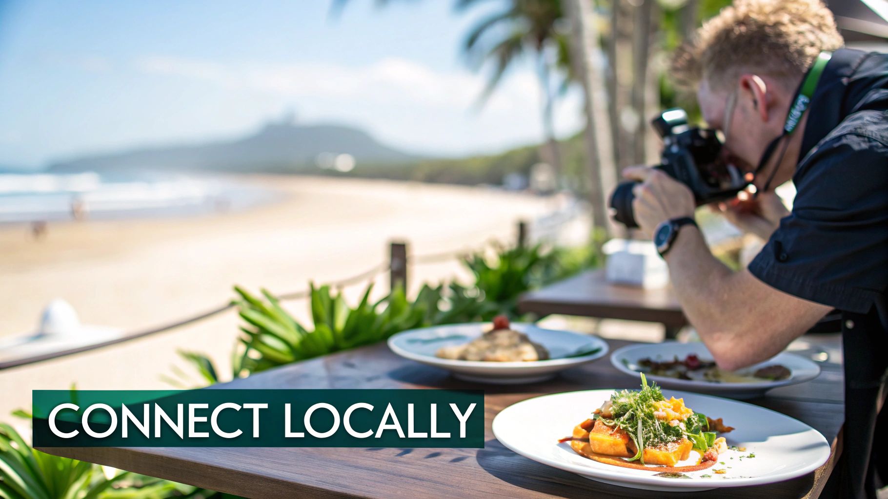 A photographer captures delicious food dishes on a table with a beautiful beach and ocean view.